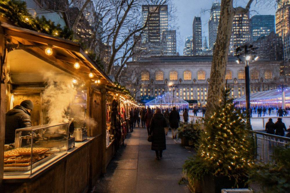 Evening view of a holiday market with a lit tree and rows of glowing vendor stalls