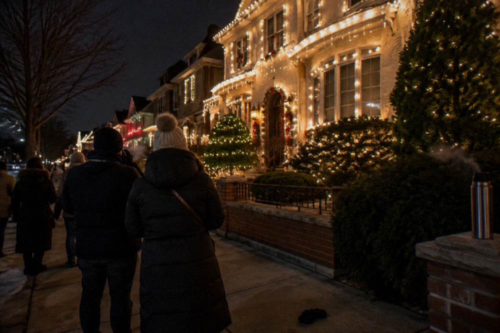 Crowded sidewalk in front of brightly decorated houses with visitors taking photos after dark