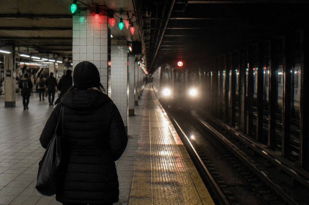 A subway platform decorated with a string of holiday lights as a train arrives at night