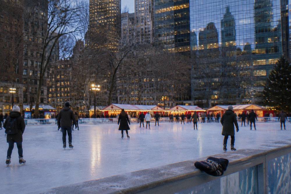Holiday market stalls glowing with string lights beside an ice rink at dusk