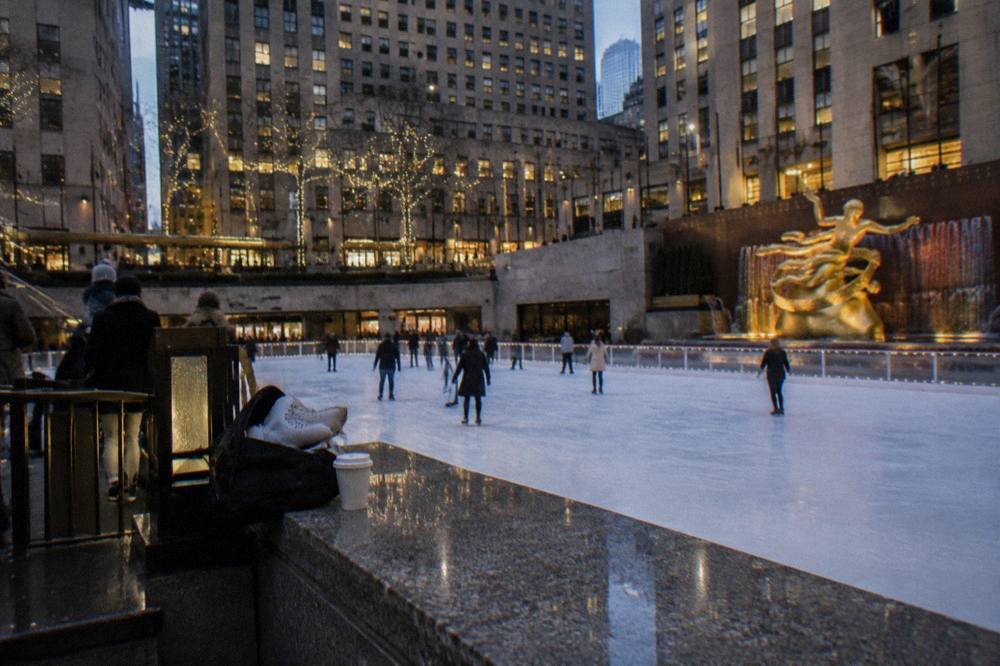 The Rockefeller Center ice rink surrounded by plaza stonework and towers at dusk