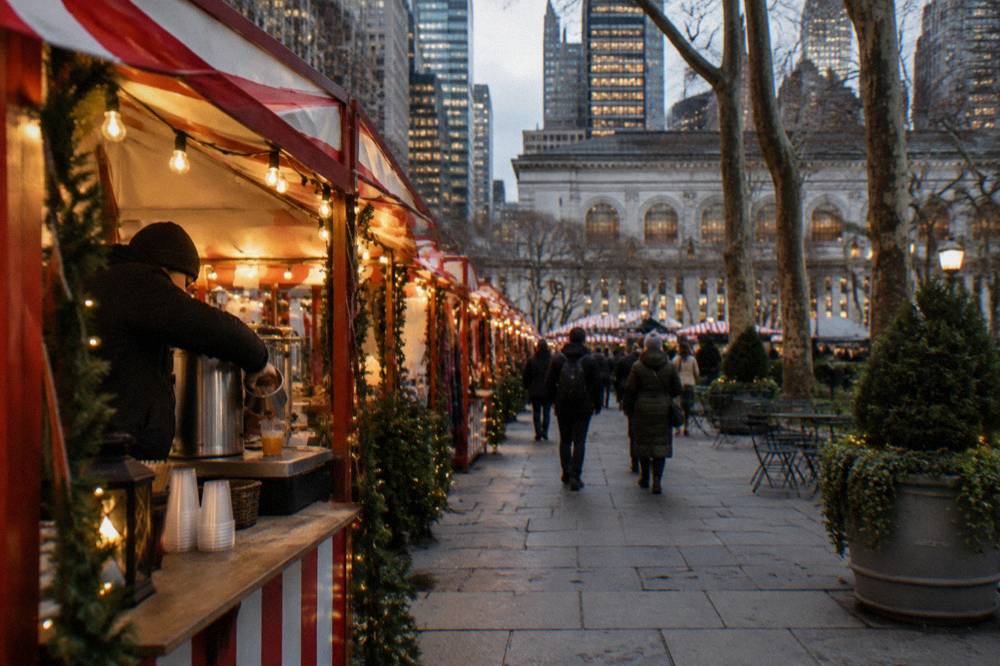 Holiday market stalls strung with lights along a Midtown walkway in the evening