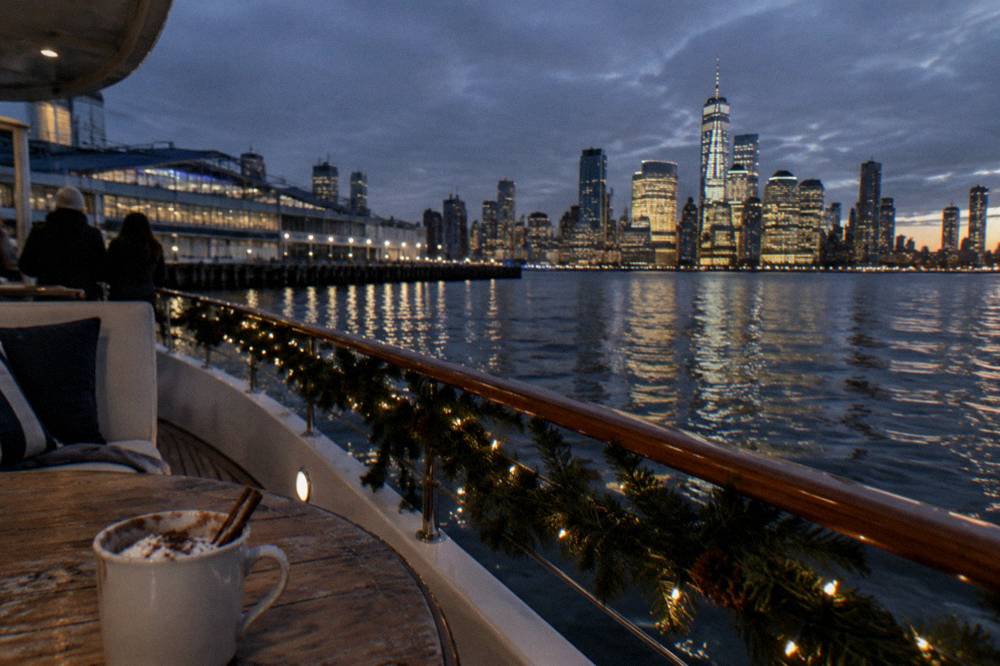 A decorated yacht passing the Manhattan skyline on a winter evening with city lights reflecting on the water