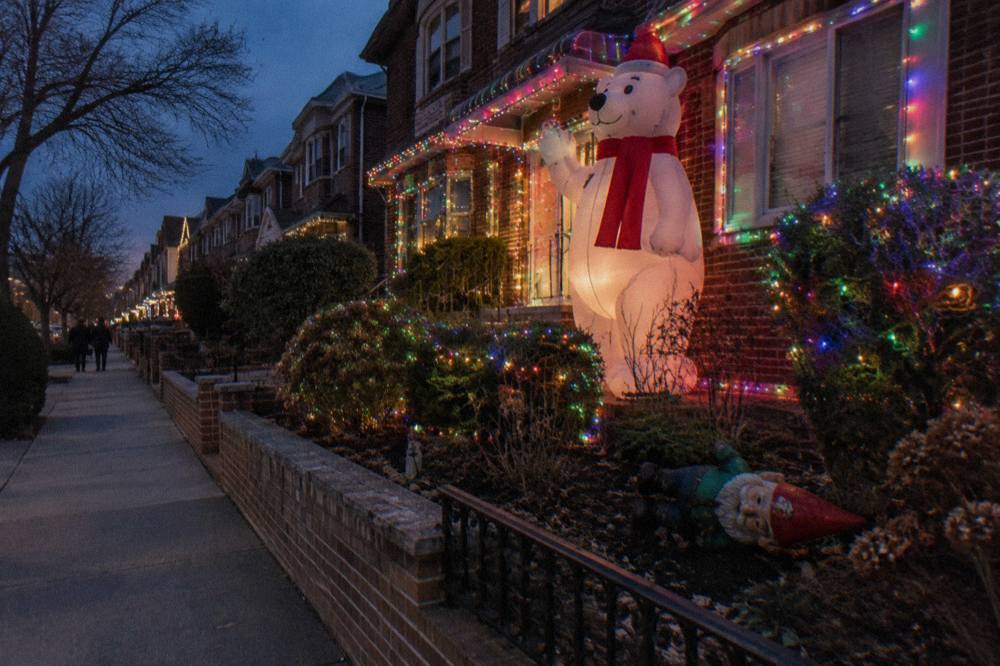 A Brooklyn residential block glowing with oversized Christmas light displays and giant holiday figures at night.