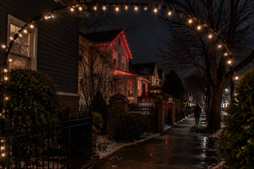 A festively lit Brooklyn street corner with strings of lights arching over the sidewalk at night.