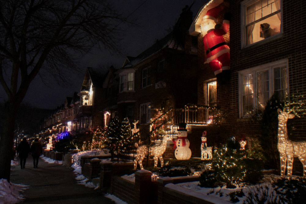 Row of Brooklyn houses decorated with illuminated reindeer, snowmen, and giant Santa figures at night
