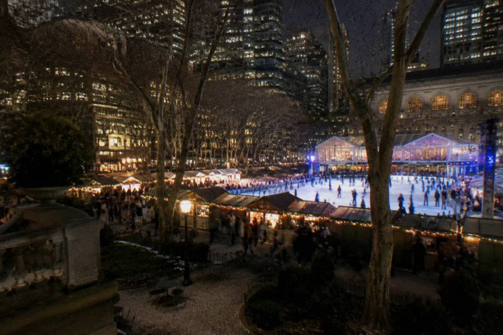 Illuminated holiday market stalls beside an ice rink surrounded by city towers at night
