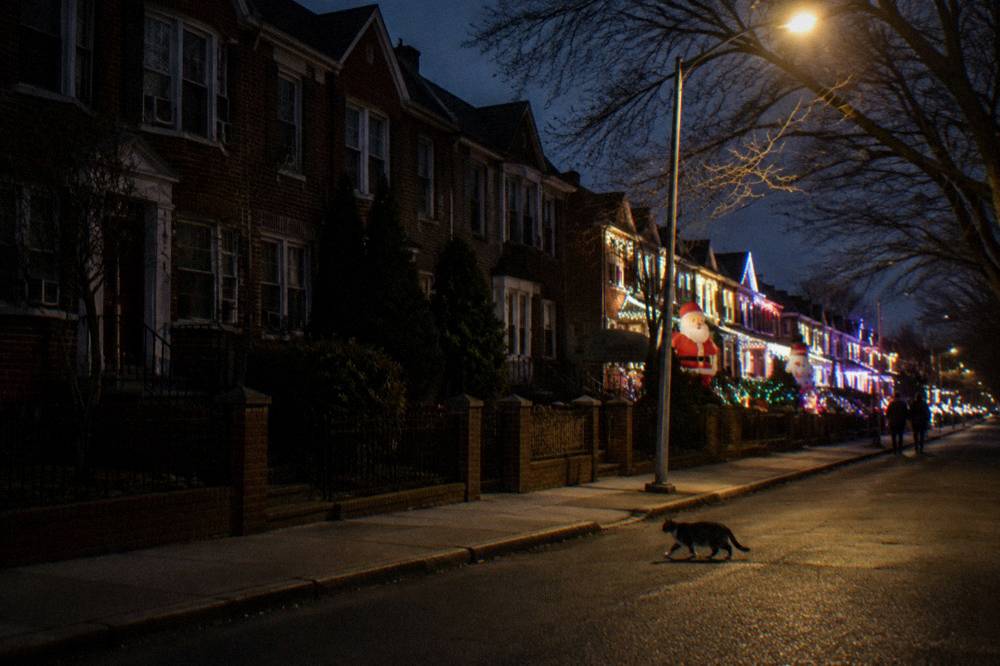 Brooklyn street at night lined with houses covered in colored string lights and inflatable holiday figures