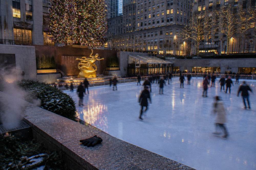 Ice rink surrounded by tall buildings and a large decorated Christmas tree in a Manhattan plaza