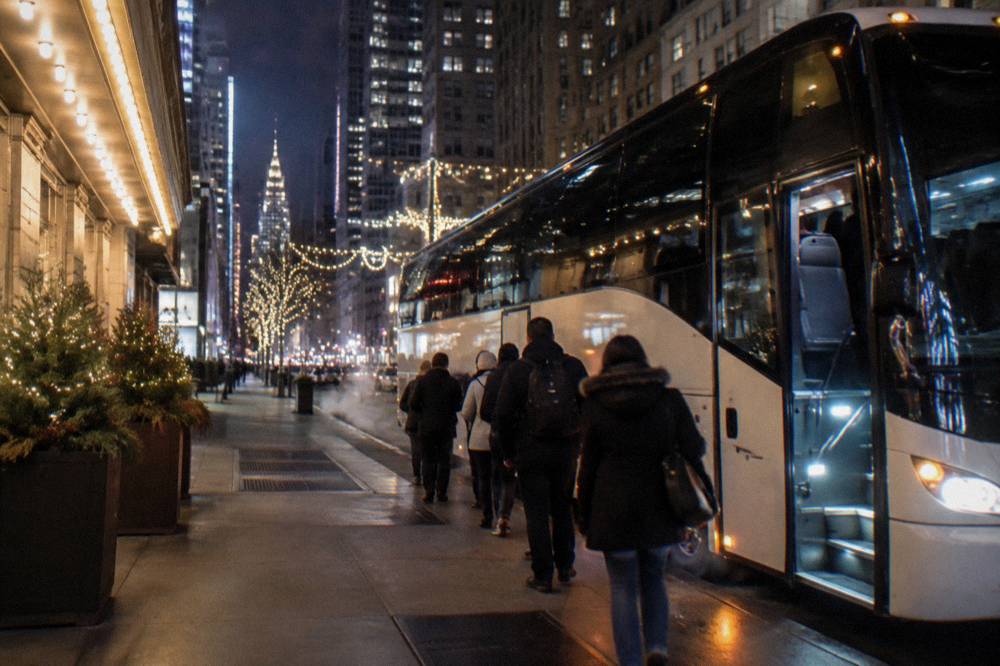 Festively decorated tour bus waiting on a Midtown street at night with holiday lights overhead