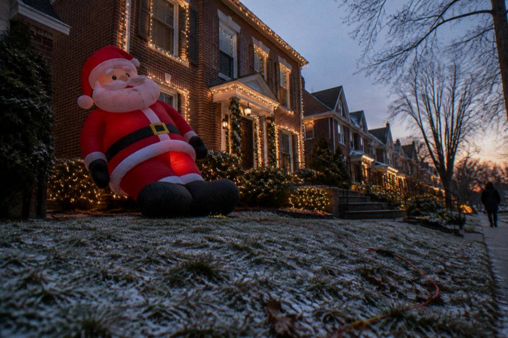 A large inflatable Santa decoration on a lit Brooklyn lawn beside a decorated house