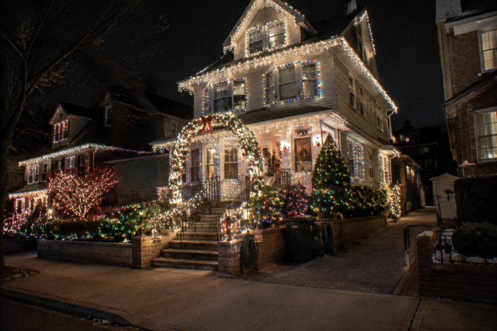A grand Brooklyn house covered in white and colored holiday lights with a lit archway