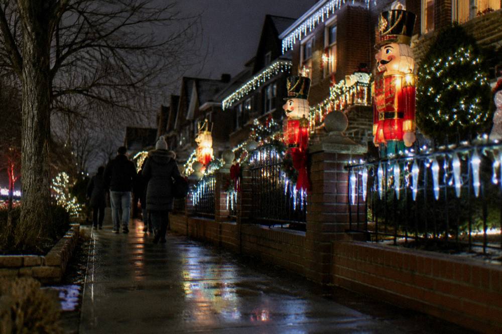 A guided walking group moving along a sidewalk past heavily decorated Brooklyn homes at night