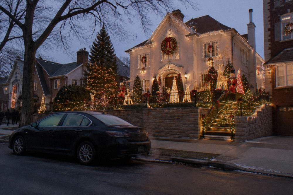 A private car parked on a quiet Brooklyn street beside homes covered in elaborate Christmas light displays