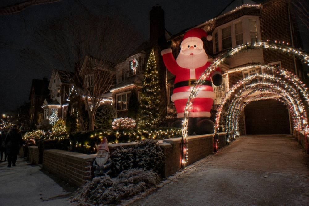Giant inflatable Santa Claus and glowing light arches on a decorated Brooklyn residential street