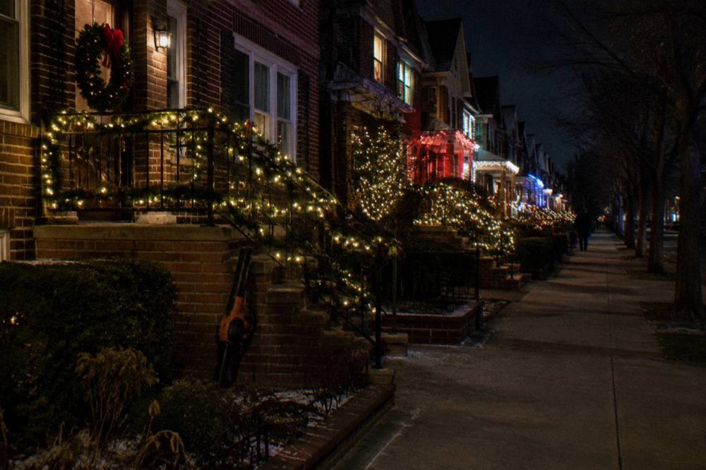 Row of brownstones covered in layered white and colored Christmas lights at night