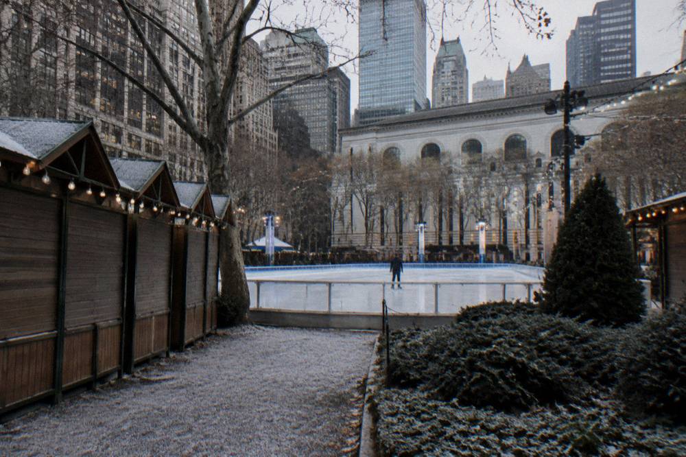 Holiday market stalls with string lights around an ice rink in a city park
