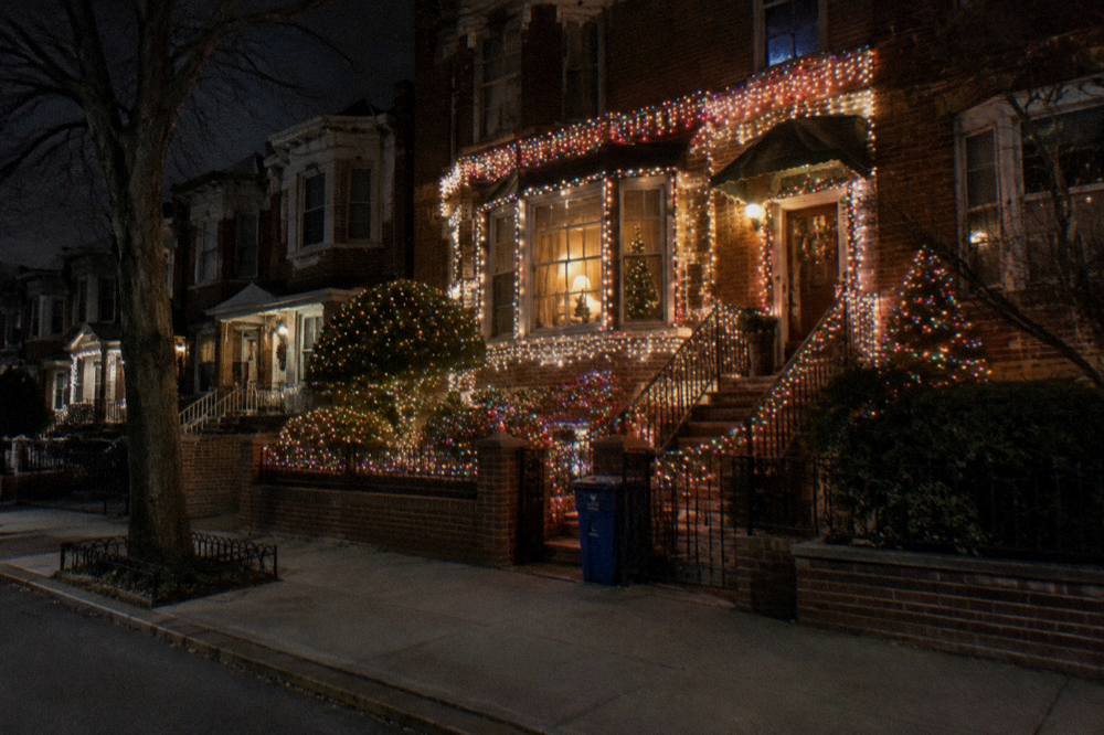 A Brooklyn street lined with brightly lit rowhouses and holiday displays at night