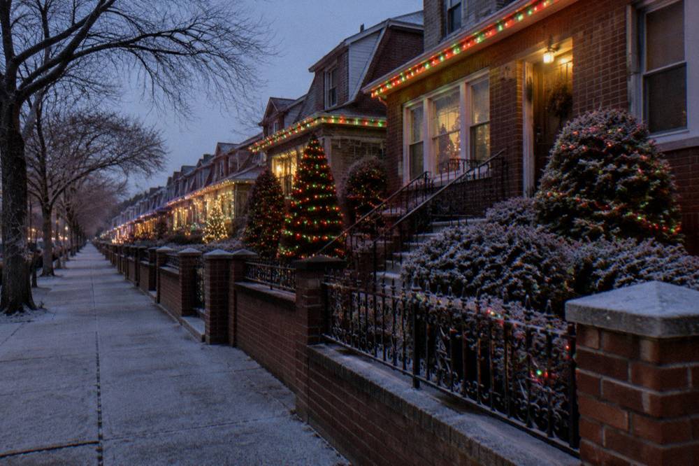 A crowd-free Brooklyn sidewalk at night with houses glowing with synchronized Christmas lights