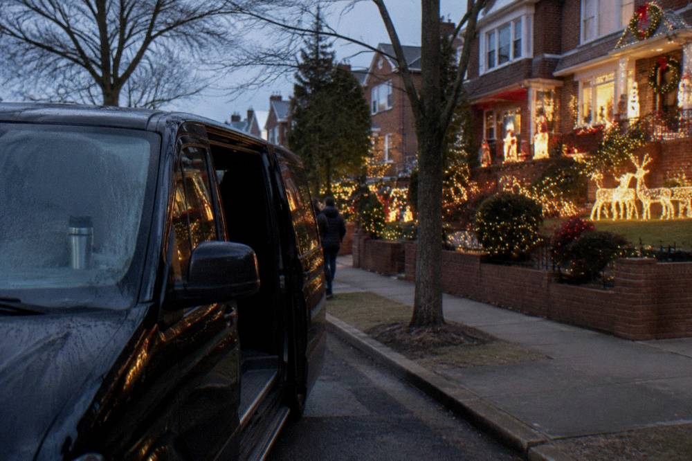 A private van parked on a festive Brooklyn street beside glowing holiday displays
