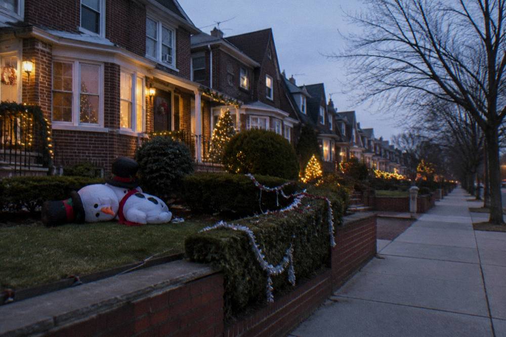 Rows of Brooklyn houses covered in oversized illuminated Christmas decorations on a residential street at dusk