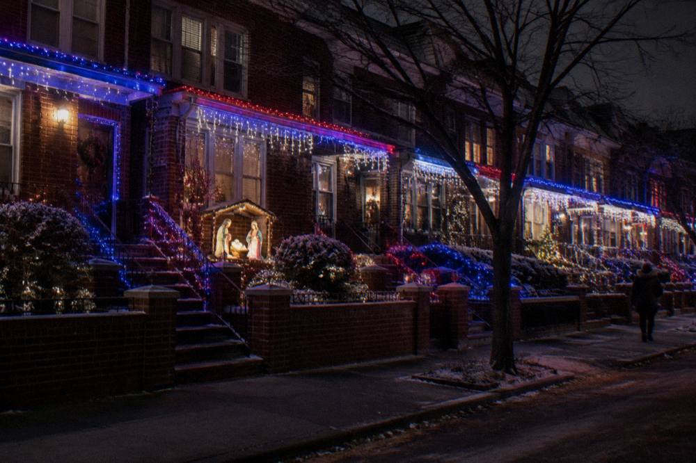 Facades of Brooklyn rowhouses covered in dense strings of colored holiday lights at night