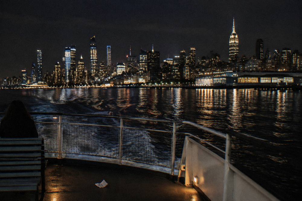 The Manhattan skyline at night seen from the water, office towers lit and reflections stretching across the river