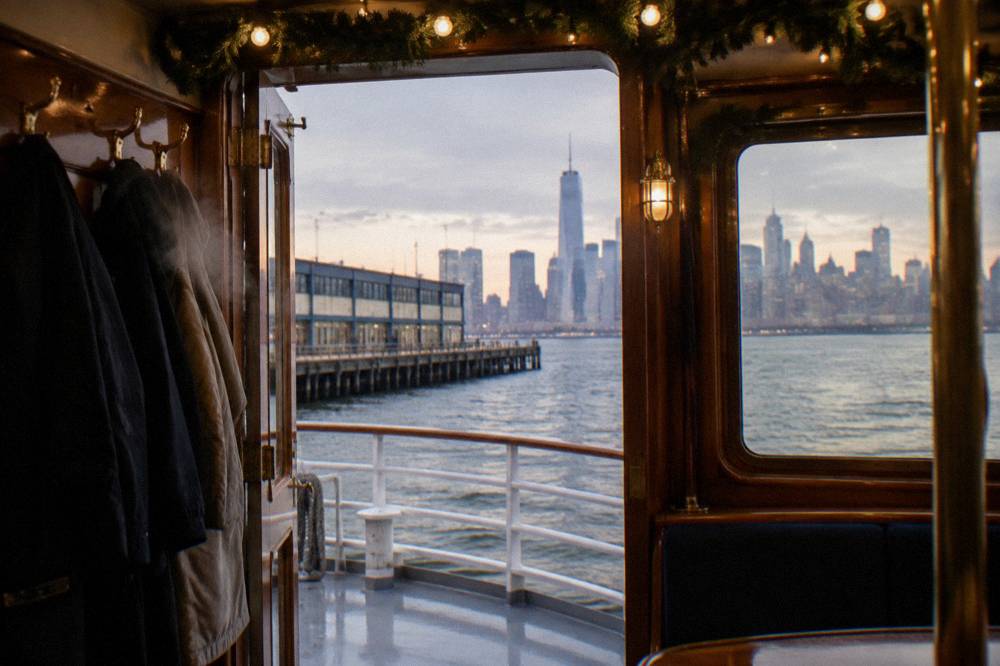 Festively lit yacht interior with garland along the ceiling and city lights visible through the windows