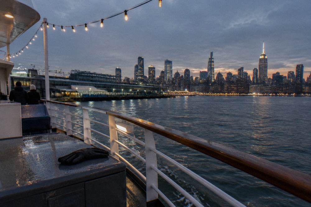 Manhattan skyline glowing at dusk seen from the Hudson River with holiday lights along the waterfront