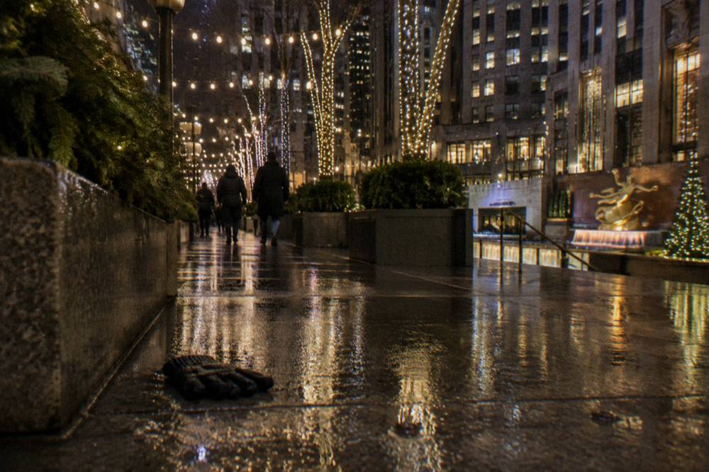 Strings of white holiday lights glowing above a Manhattan sidewalk at night