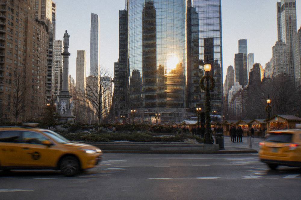 A plaza entrance with holiday banners and a glass office tower above Columbus Circle in late afternoon