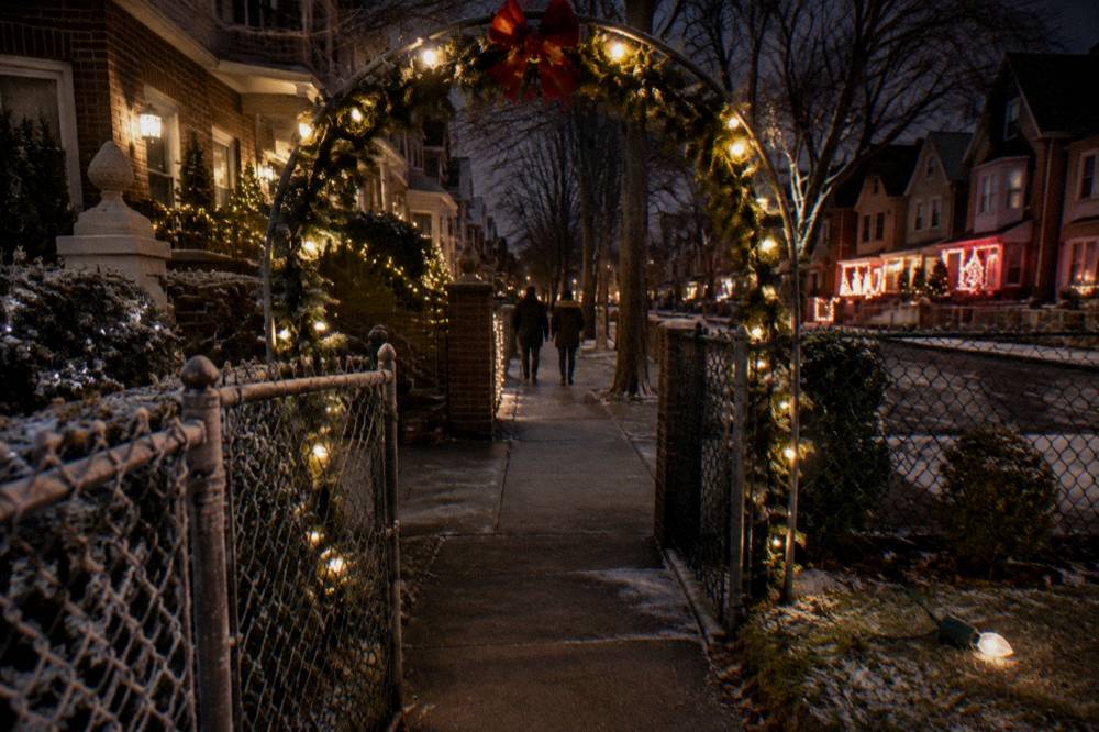 Glowing holiday light archway over a quiet Brooklyn sidewalk at night