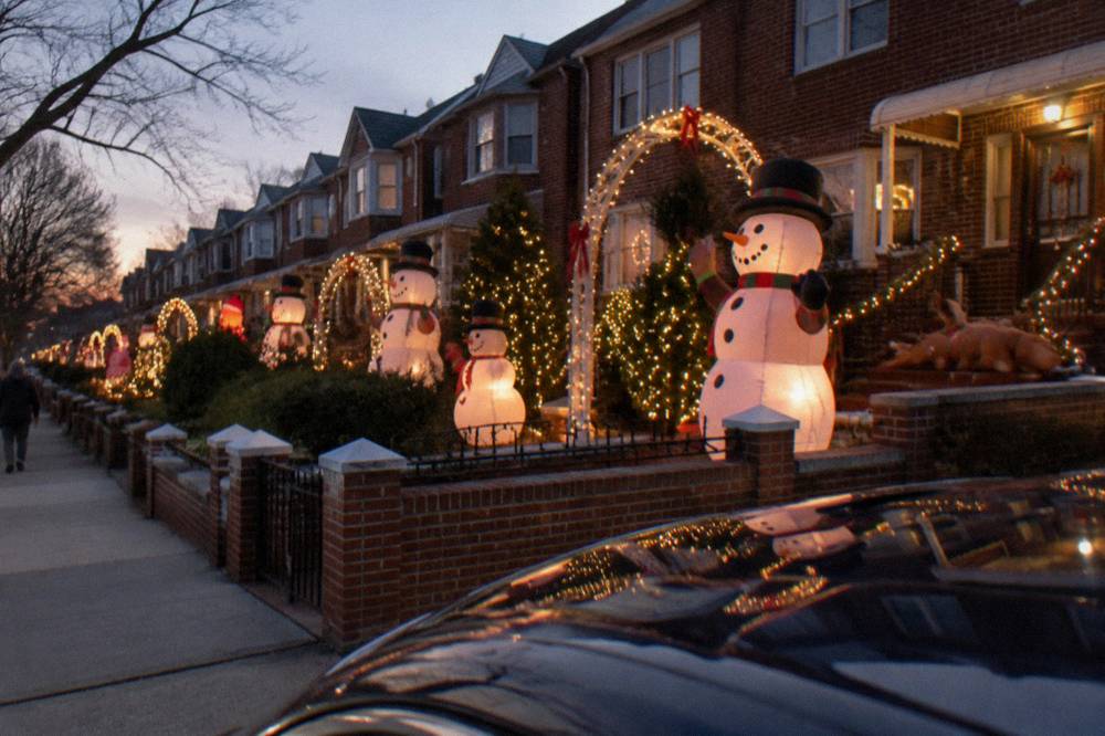 Rows of decorated houses with inflated snowmen and lighted arches along a quiet residential street in Dyker Heights