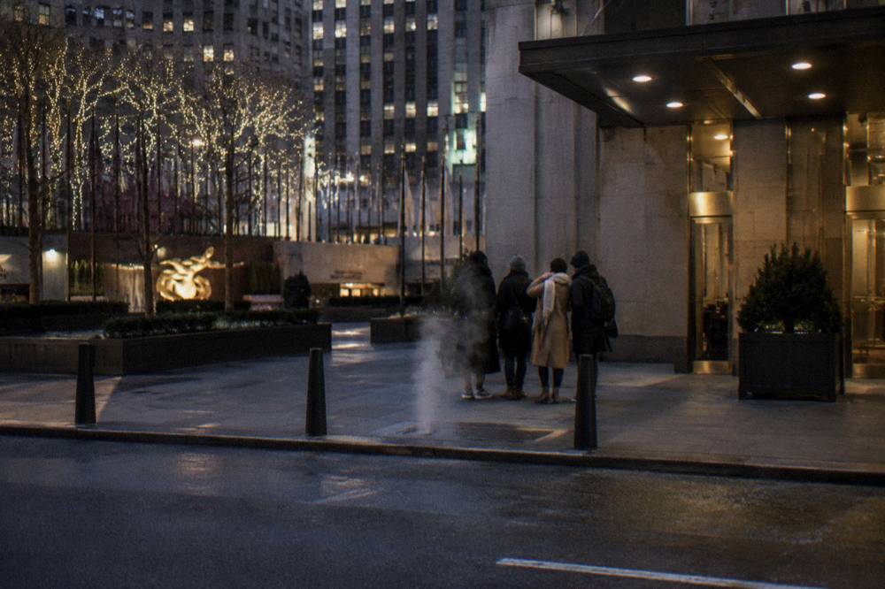 Small guided walking tour gathered on a festively lit sidewalk in Midtown Manhattan at night