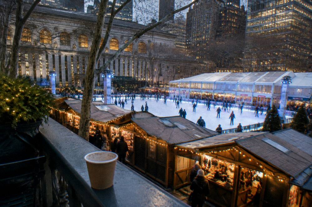 Ice rink surrounded by holiday market stalls and glowing lights in Bryant Park in the evening