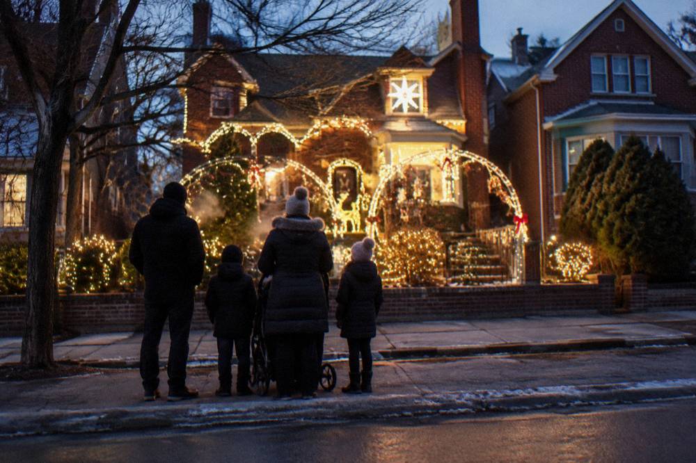 Family group in winter coats viewing a brightly lit private home display on a Brooklyn street