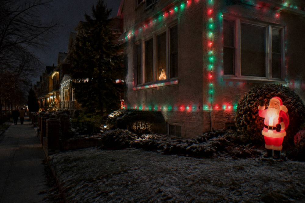Close view of a corner house covered in synchronized colored holiday lights and a lit Santa figure