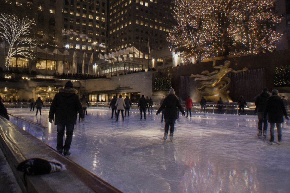 Skaters on an ice rink beneath a large lit Christmas tree at night