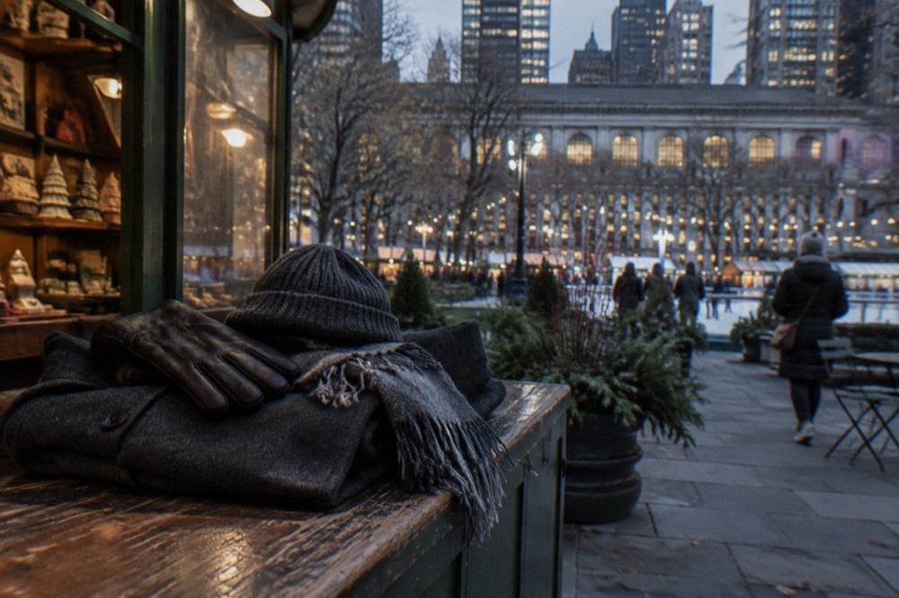 A folded wool coat with scarf, gloves and knit hat resting on a wooden bench