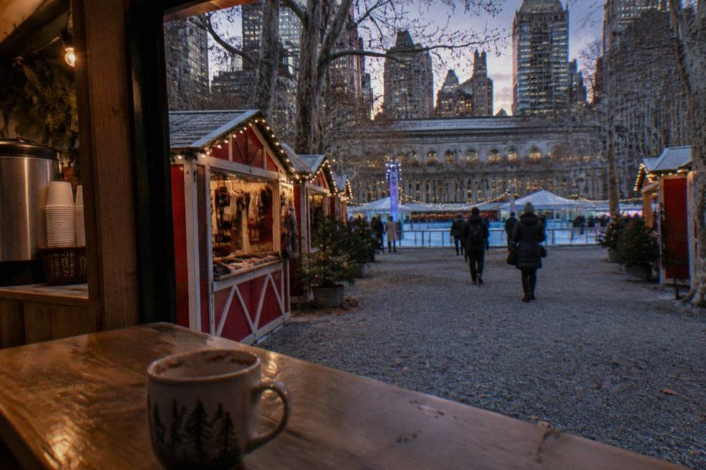 Open-air holiday market stalls with string lights beside an ice rink
