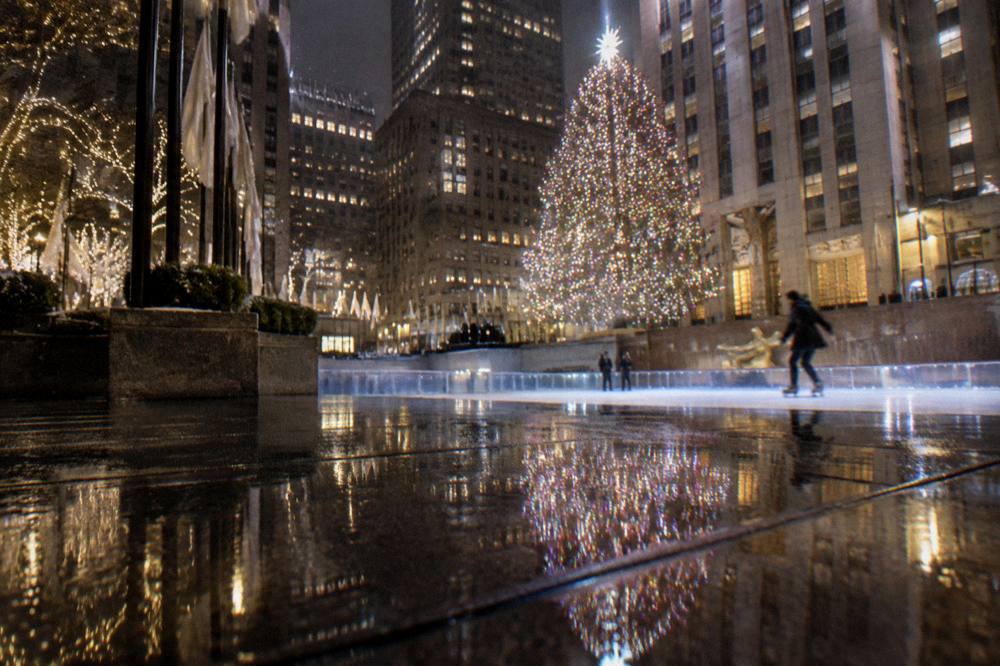 Open plaza at night with a large lit Christmas tree reflected in wet pavement
